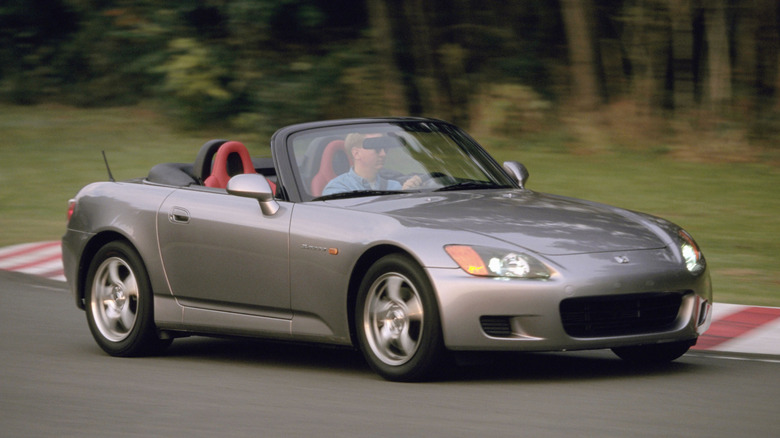 Передня тричетвертна частина сріблястої Honda S2000, що їде поворотом на гоночній трасі повз траву та дерева
