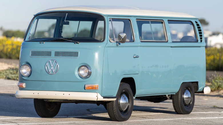 Світло-блакитний VW Bus 1968 року, припаркований на асфальті перед зеленими кущами