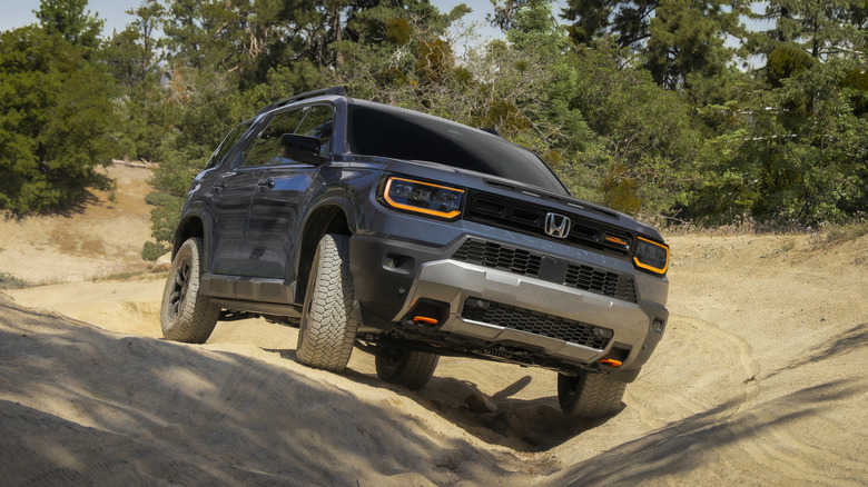 Синій Honda Passport TrailSport їде по коліїйній ґрунтовій дорозі перед деревами.