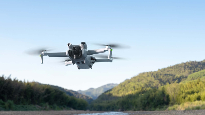 Дрон DJI Mini 3 летить над водою з горами та синім небом на задньому плані
