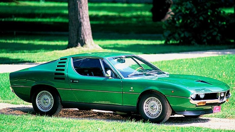 Смарагдово-зелений спортивний автомобіль Alfa Romeo Montreal, припаркований на гравійній під'їзній дорозі на галявині.