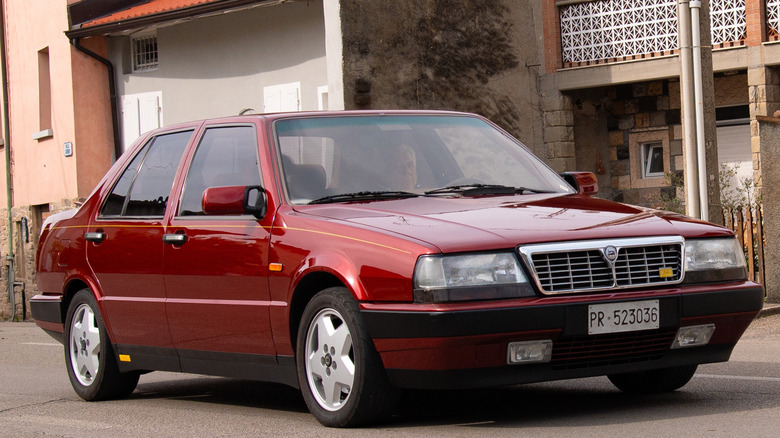 Lancia Thema 8.32 темно-червоного кольору, припаркований біля низки будинків