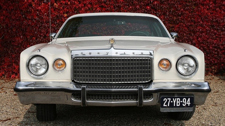 Передня частина білого Chrysler Cordoba на тлі стіни з червоного плюща.