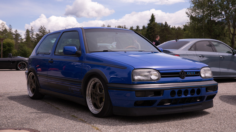 Синій Volkswagen GTI на автозустрічі на тлі хмарного неба.