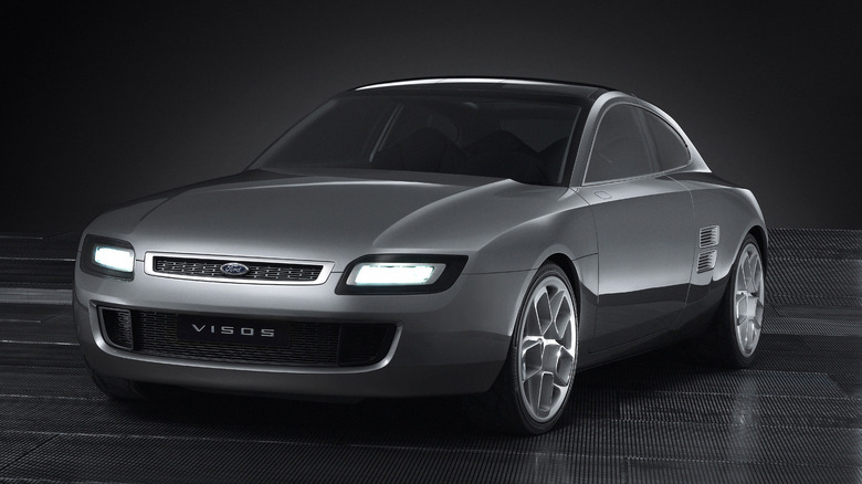 Сріблястий купе-концепт 2003 Ford Visos, що підкреслює його силует фастбек, натхненний Capri, вузьку верхню решітку з підсвіченими прямокутними фарами, жалюзі на задніх крилах і виліплені багатоспицеві легкосплавні диски на темному тлі.