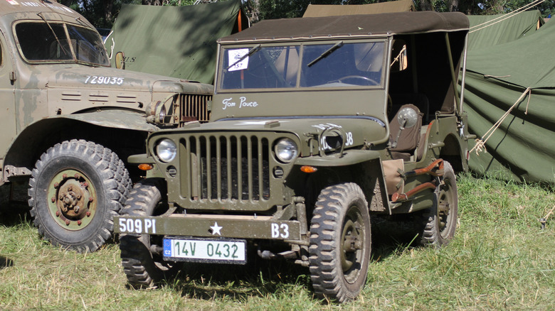 Військовий джип Willys, припаркований на траві, поряд з іншою військовою технікою.