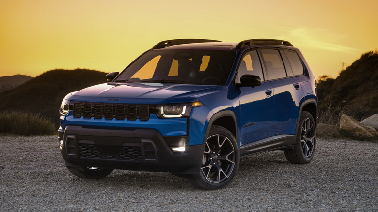 Синій Jeep Cherokee 2026 року на гравійній дорозі під час золотого часу з пагорбами на задньому плані.