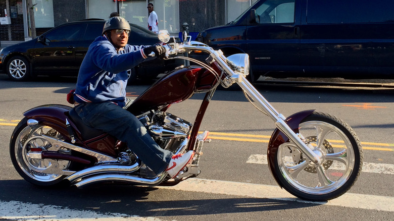 A motorcycle rider sits on a chopper-style bike in profile, showing steering geometry.
