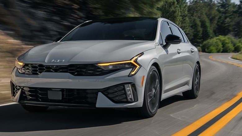 Сіра Kia K5 2026 року в русі на дорозі.