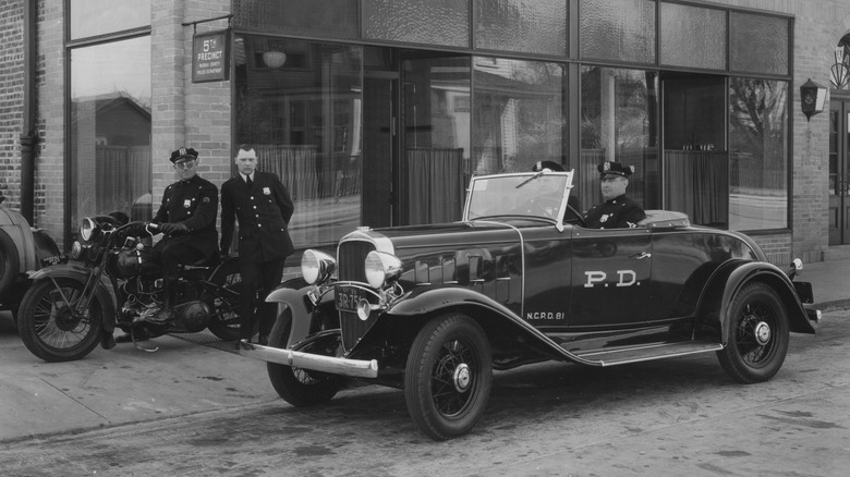 Чорно-біла фотографія офіцерів у поліцейському автомобілі та на мотоциклах біля поліцейського відділку у 1929 році.