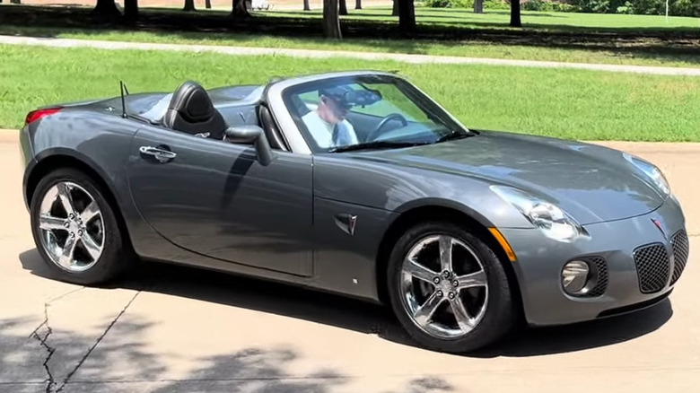 Сірий родстер Pontiac Solstice GXP їде з опущеним верхом по асфальтованій доріжці.