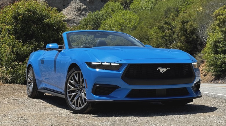 Передньо-бічний вид яскраво-синього Mustang EcoBoost кабріолета, припаркованого на ґрунтовій дорозі з опущеним верхом на тлі гір.