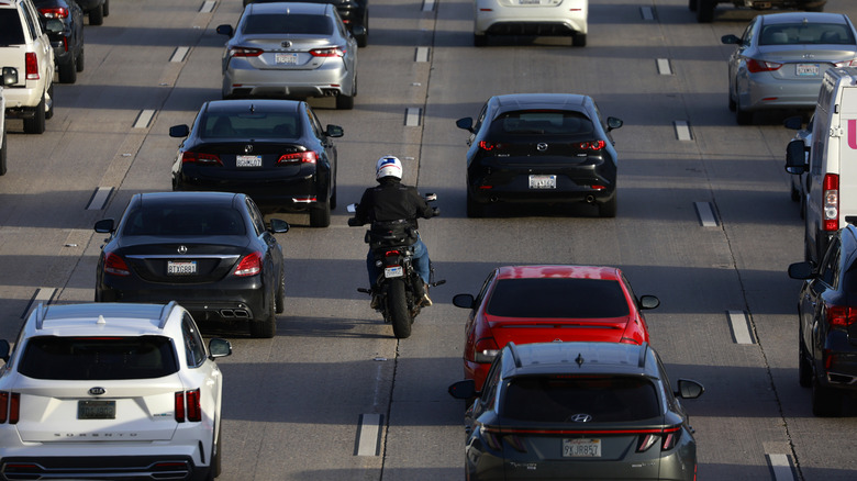A motorcycle slips between cars in traffic riding on the lane markers.