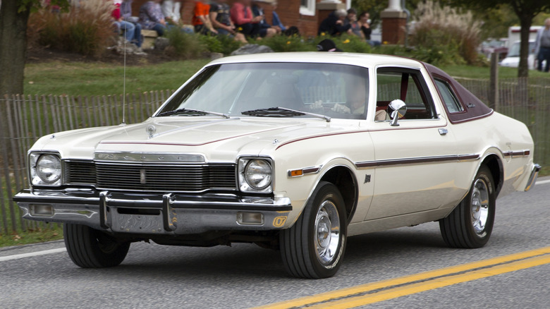 Білий Dodge Aspen кінця 1970-х років з вініловим дахом кольору бургундського вина та масивними хромованими бамперами, що їде по дорозі.