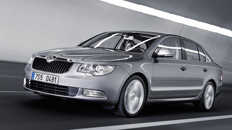 Сріблястий Skoda Superb рухається через освітлений тунель, світло відбивається від блискучої поверхні автомобіля.