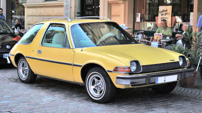 Яскраво-жовтий AMC Pacer хетчбек з його характерним скляним куполом, припаркований на бруківці.