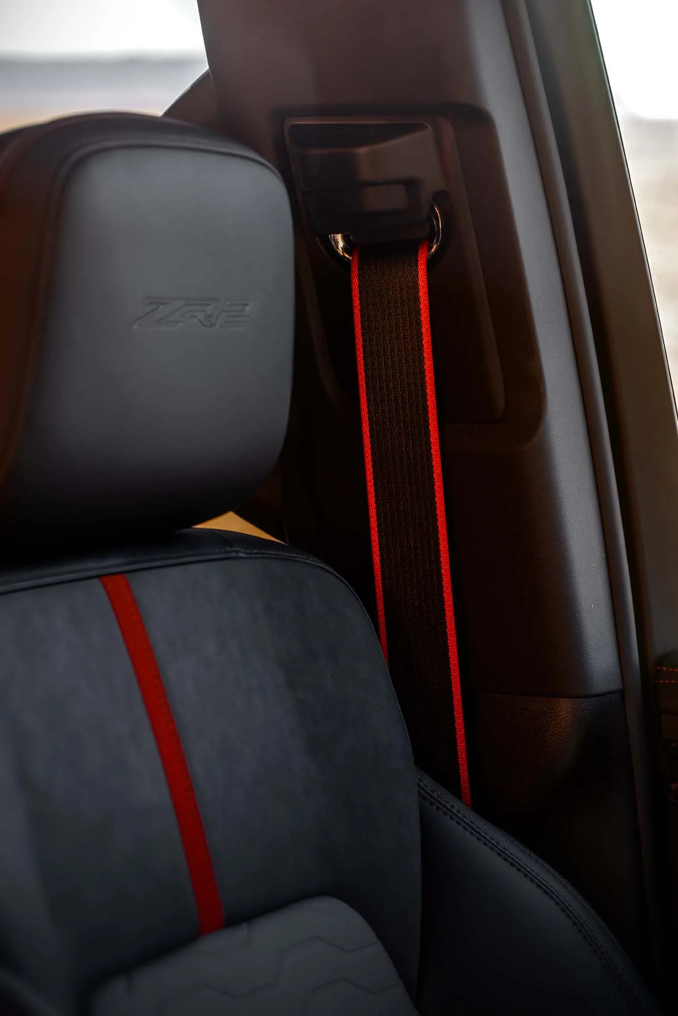 2027 Chevrolet Silverado 1500 ZR2 з інтер'єром Dark Galvinized. Детальний знімок переднього сидіння, що демонструє червону обробку Torch Red, ремінь безпеки з червоним кантом та вибитий логотип ZR2 на підголівнику.