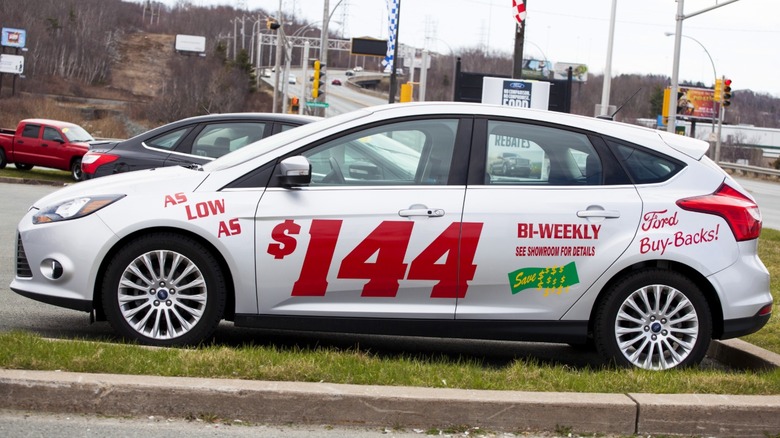 Автомобіль з низькою щодвотижневою ціною, намальованою на боці, припаркований на майданчику дилера