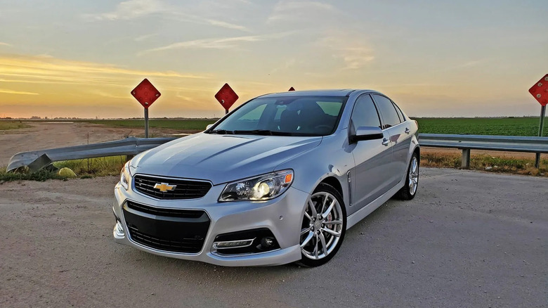 Сріблястий Chevrolet SS, припаркований на асфальті перед кінцем дороги з червоними знаками, зеленим полем та відкритим небом у сутінках