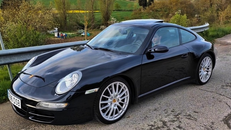 Porsche 911 Carrera 4 чорного кольору, припаркований на асфальтованій дорозі біля металевого відбійника.