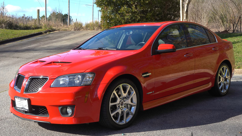 Яскраво-червоний седан Pontiac G8 GXP підвищеної потужності з повітрозабірниками на капоті та легкосплавними дисками, припаркований на стоянці.