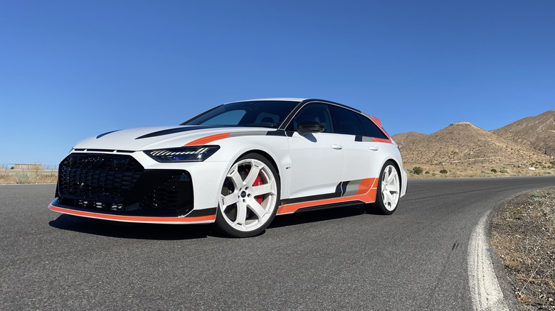 Передня тричетвертна частина білого Audi RS6 Avant GT, припаркованого на трасі Willow Springs Raceway на тлі синього неба та гір