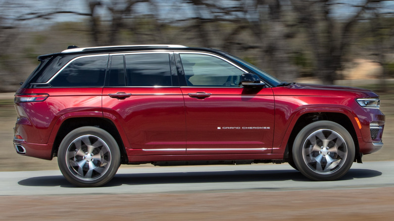 Червоний Jeep Grand Cherokee 2022 року їде дорогою повз голі дерева.