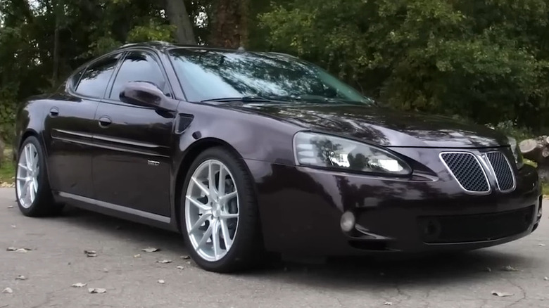 Темно-фіолетовий седан Pontiac Grand Prix GXP 2005-2008 років зі сріблястими багатоспицевими дисками на асфальтовій дорозі.