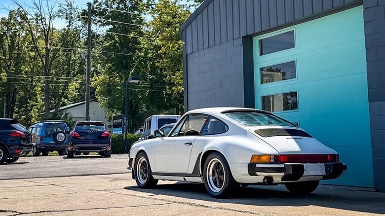 Задній вид з 3/4 білого Porsche 911 SC 1982 року, припаркованого перед гаражними дверима