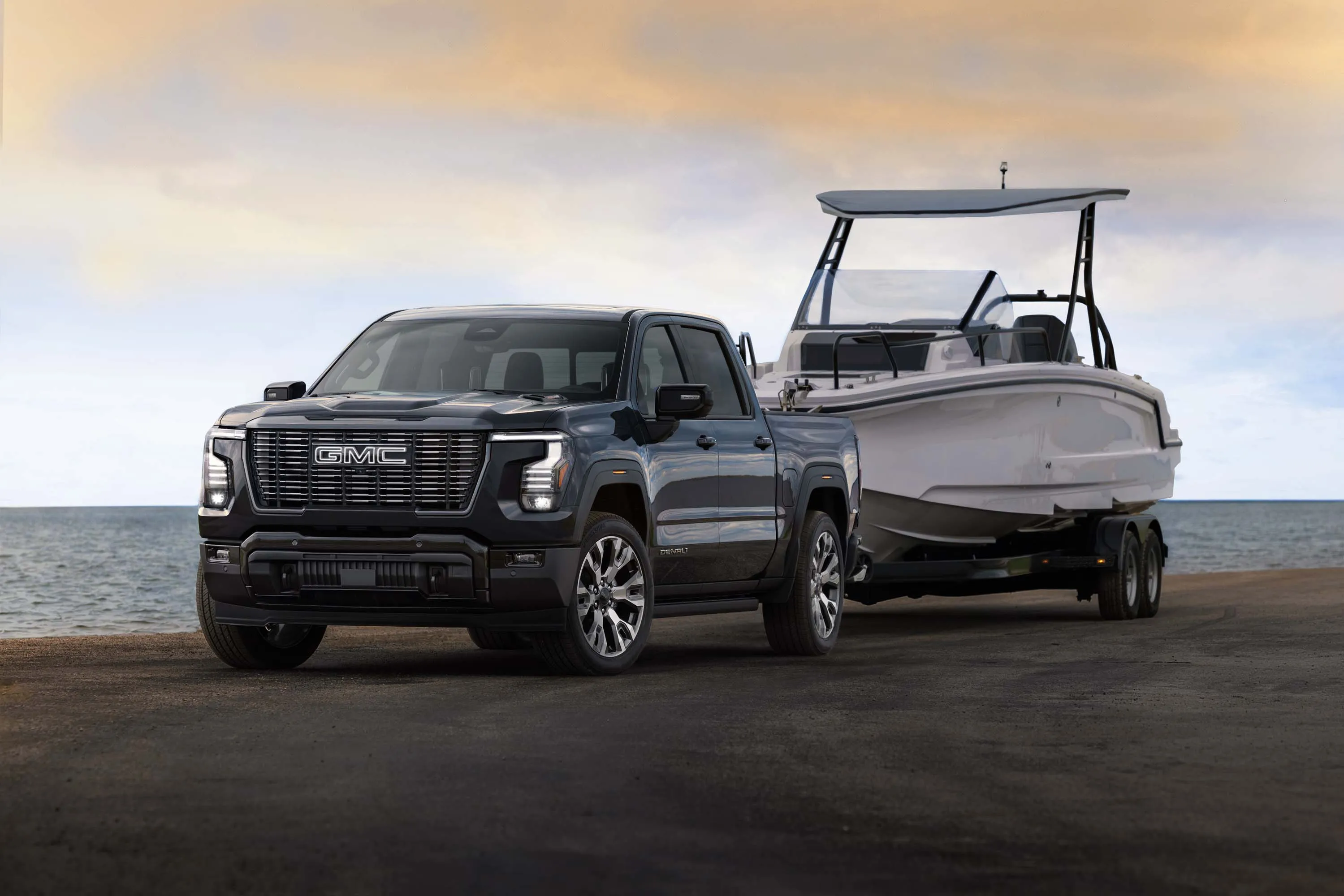 2027 GMC Sierra 1500 Denali Ultimate в кольорі Dark Ridge Metallic, що тягне човен. Зовнішній вигляд 3/4. Показано передсерійну модель. Фактична серійна модель може відрізнятися.