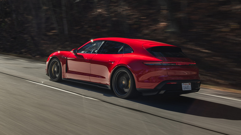 Задня тричетвертна частина червоного Porsche Taycan Sport Turismo, що їде повз темні дерева