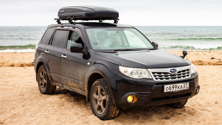 Чорний Subaru Forester із прикріпленим зверху багажним боксом на піщаному пляжі.