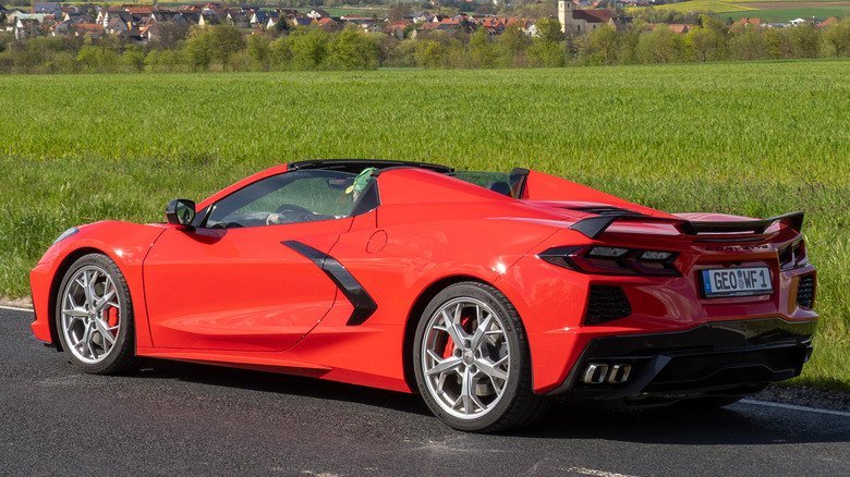Червоний Corvette C8 припаркований на сільській дорозі поруч із зеленим полем.